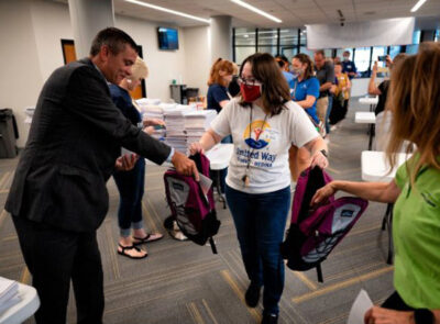 A woman handing out backpacks with supplies