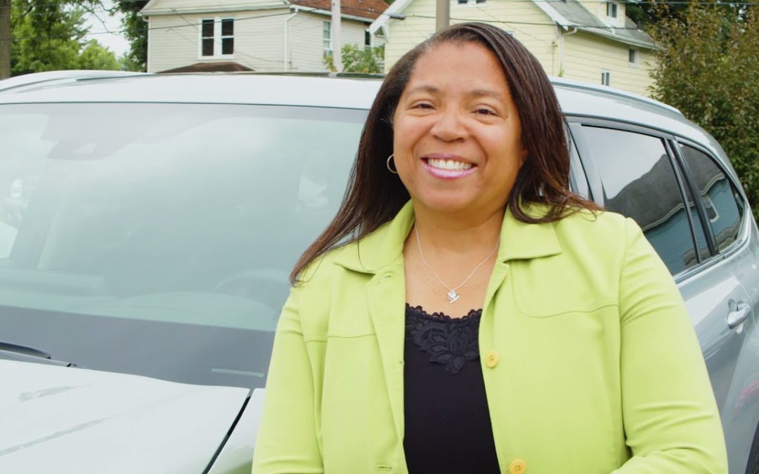 A woman standing outside of her car, smiling, posing for the photo